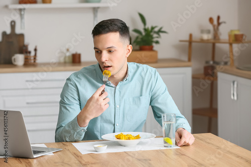Young man with laptop eatin...