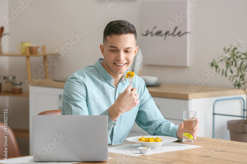 Young man with laptop eatin...