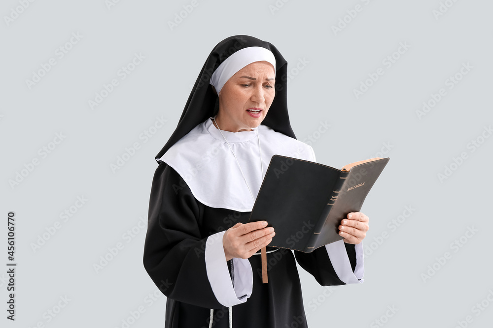 Mature nun reading Holy Bible on light background