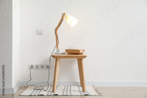 Glowing lamp and books on table near light wall