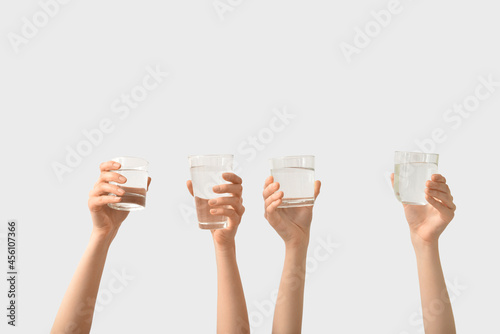 Female hands with glasses of water on light background