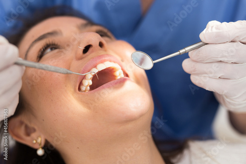 Close up hands of dentist in the gloves holding dental probe and intraoral mirror near woman teeth