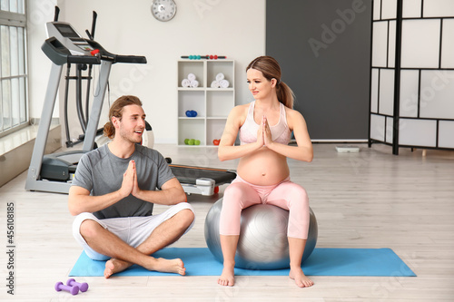 Young pregnant woman and her husband with fitball training in gym