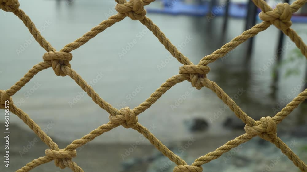 Rope Net Fence On Seashore Of Beach With Calm Water In The Background. - closeup