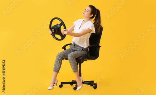 Young woman with steering wheel sitting in chair on color background © Pixel-Shot