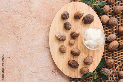 Wooden board with shea butter and nuts on color background, closeup