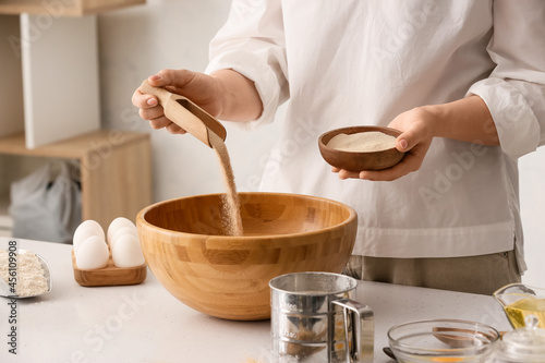 Fotografija Female chef adding dry yeast in bowl on kitchen table, closeup