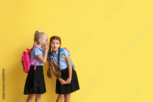 Cute gossiping schoolgirls on color background