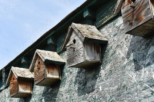 An image of several home made wooden bird houses lined up on the exterior of a run down building. 