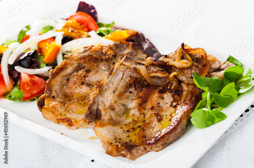 Appetizing grilled pork chop with fresh colorful salad of vegetables decorated with cornsalad leaves