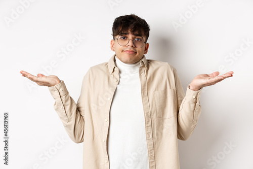 Portrait of handsome young man looking confused, know nothing, shrugging shoulders and spread hands sideways clueless, standing on white background photo