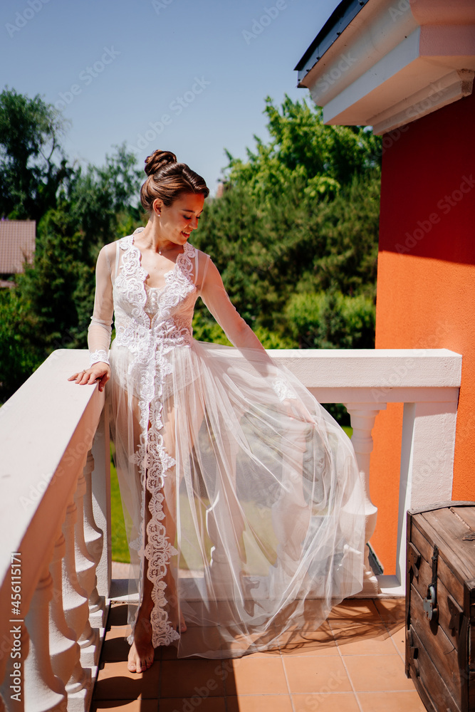 Fototapeta premium a beautiful bride in a transparent lace robe stands on the terrace. 