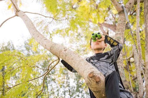 Little batman boy climbing a tree in the garden looking through a binocular photo