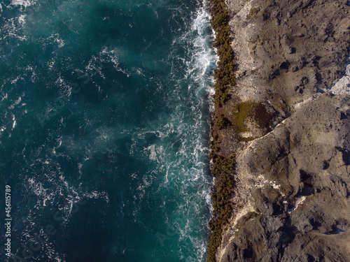 Seascape. Dark turquoise ocean water with light white waves and rocky coast. Beauty of nature. View from above. Drone shooting. Ecology, tourism, recreation, the greatness of nature.