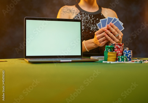 An elegant woman in an evening dress plays poker in an online casino. She has cards in her hands, stacks of chips on the table, an open laptop. Gambling, online casino, gambling business.