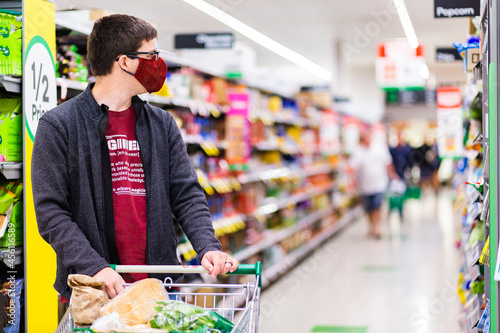 Young male person grocery shopping for essentials with face mask protection from spreading covid-19 photo