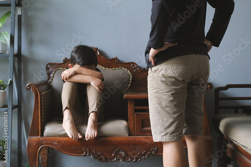 A Little Asian boy crying on the sofa while being scolded by someone stands in front of him. Bullying, discrimination, and racism concept
