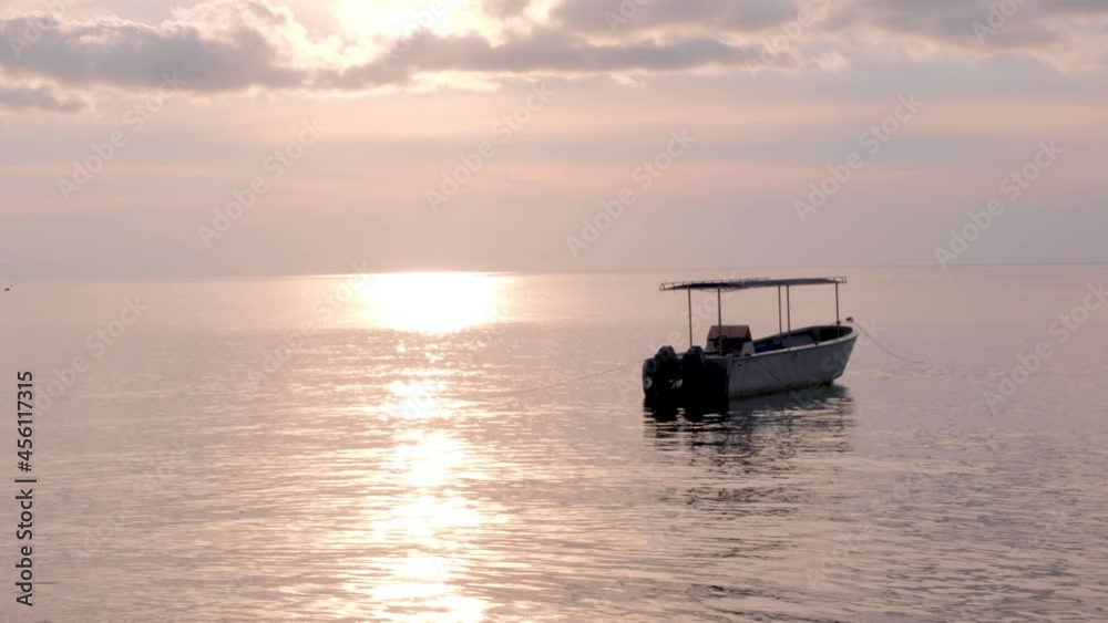 A solo dive motorboat anchored near coral reef with stunning pink hue sunset over ocean at Atauro Island in Timor Leste, Southeast Asia A solo dive motorboat anchored near coral reef with stunning pink hue sunset over ocean at Atauro Island in Timor Leste, Southeast Asia