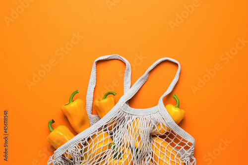 Gray mesh bag with ripe bell pepper on an orange background. Vegetarian food.