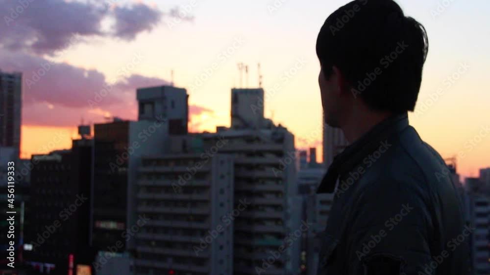 Man on rooftop looking at sunset and city buildings in Tokyo Man on rooftop looking at sunset and city buildings in Tokyo