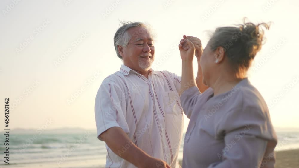 Happy Asian family senior couple holding hand and dancing on the beach together at summer sunset. Elderly retired husband and wife relax and enjoy romantic outdoor holiday vacation with happiness Happy Asian family senior couple holding hand and dancing on the beach together at summer sunset. Elderly retired husband and wife relax and enjoy romantic outdoor holiday vacation with happiness
