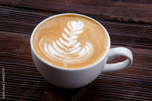 cup of hot cappuccino with pattern on wooden background 