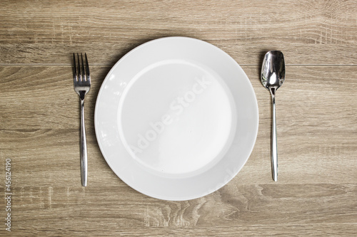 A white plate with spoon and fork on a wooden table.