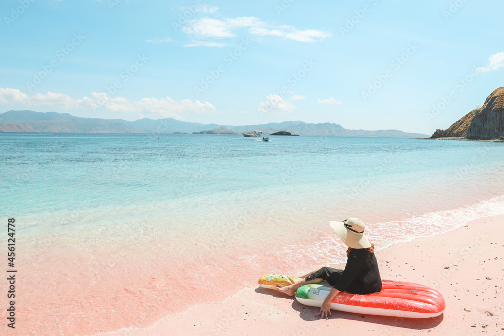 A girl in summer hat sitting on inflatable mattress while enjoying sea view in pink sandy beach