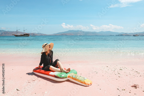 Blonde woman in summer hat and sunglasses relaxing on inflatable mattress in pink sandy beach