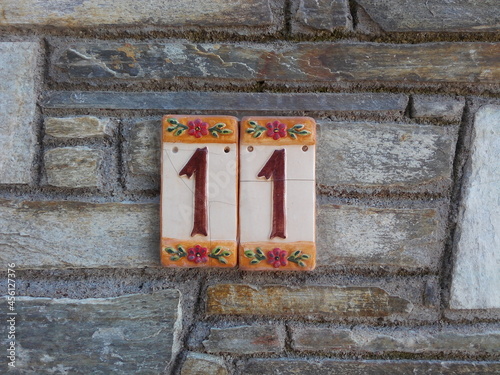 House number 11: red figures on cracked ceramic plaques decorated with flowers against a stone wall photo