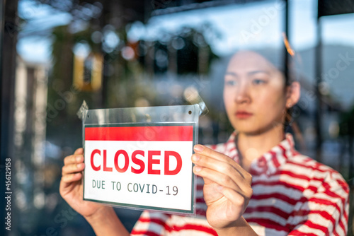An upset Local small business owner woman or waitress is putting the sign for "sorry we closed" in front of the cafe, coffee shop, or retail store glass door cause lockdown quarantine due to covid-19 © tai