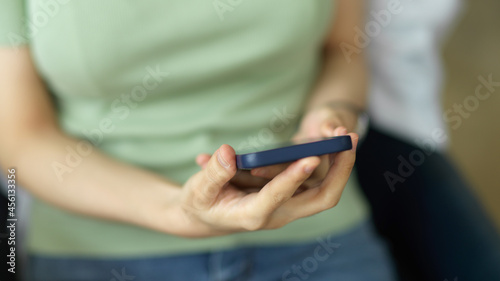Closeup young female in pastel green comfy shirt sitting and holding mobile phone