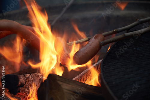 Multiple hot dogs on sticks being grilled outdoor over an campfire