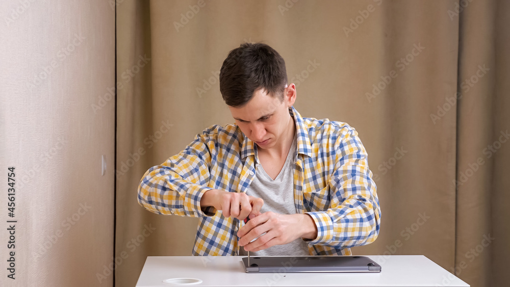 Young man disassembles a laptop with a screwdriver while sitting at table. Young man disassembles a laptop with a screwdriver while sitting at table.