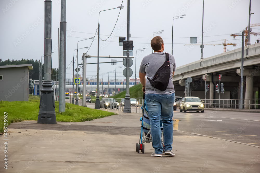 Father with son in a stroller walk along the sidewalk in the vicinity of the city. A child in a baby carriage and a man in the background of nature. Family holiday on a vacations.