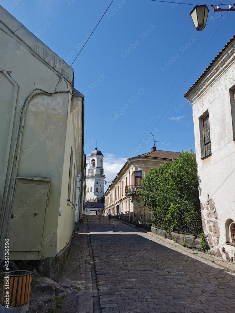 A cobblestone street leading to the Clock Tower, a former bell tower, in the city of Vyborg against the blue sky. A cobblestone street leading to the Clock Tower, a former bell tower, in the city of Vyborg against the blue sky.