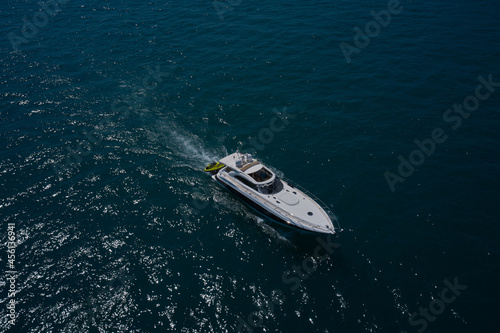 The yacht is fast moving on dark water. Large white yacht on the water in motion top view. Luxury motor boat on dark blue water aerial view. © Berg