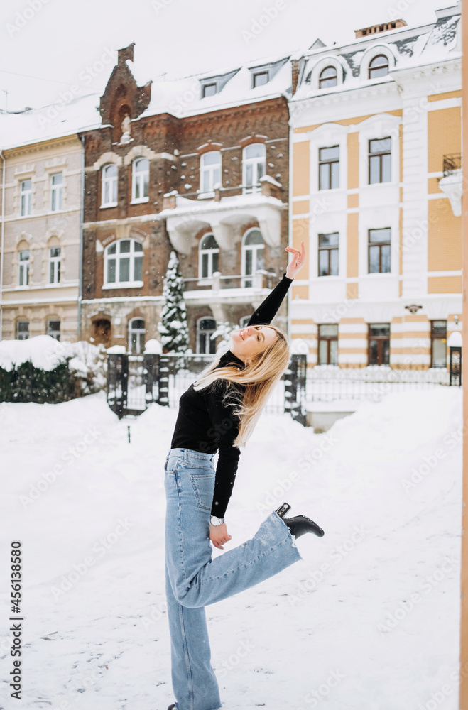 Young beautiful blonde in a black sweater and jeans posing on a background of winter street