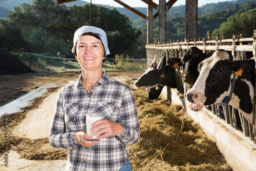 Confident positive russian female milker approvingly demonstrating milk on dairy farm