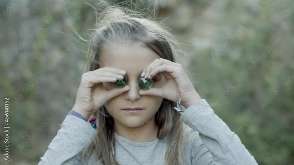 Medium shot of Caucasian girl putting stones to her eyes. Cheerful female teenager having fun during summer vacation, enjoying carefree days, mugging for camera. Abandoned castle, portrait concept Medium shot of Caucasian girl putting stones to her eyes. Cheerful female teenager having fun during summer vacation, enjoying carefree days, mugging for camera. Abandoned castle, portrait concept