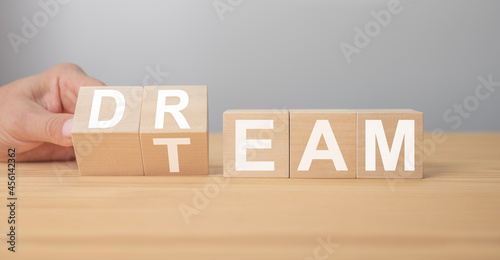 Dream team. Businessman turns cubes and changes the word dream to team. Wooden table, grey background. Business and dream team concept, copy space. photo