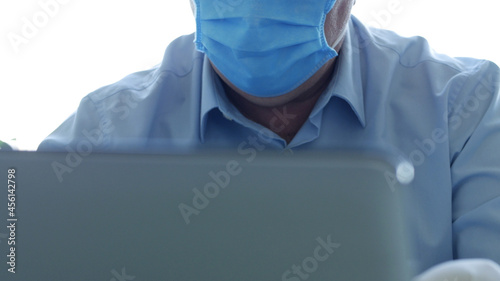 Doctor in a Hospital Office with a Face Mask and Protective Gloves Using a Laptop