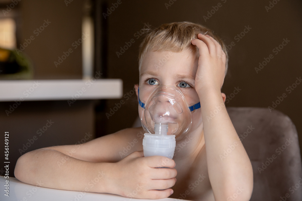 A sad little boy does inhalations with a nebulizer at home, he is sick. Help at home with cough, asthma. Concept health A sad little boy does inhalations with a nebulizer at home, he is sick. Help at home with cough, asthma. Concept health