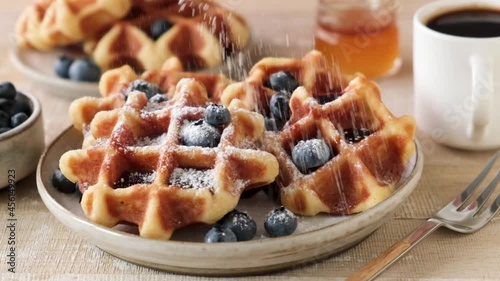 Sift confectioner's sugar on belgian waffles in slow motion. Sweet breakfast food, closeup view of yummy crispy waffles photo