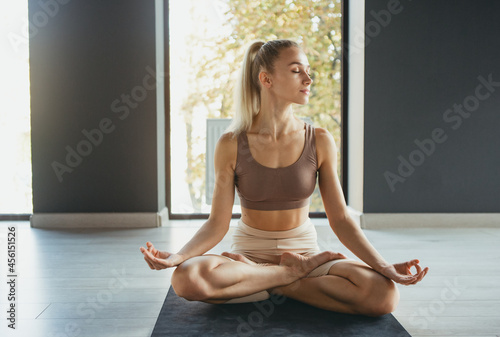 Portrait of young slim sportive woman in sportswear doing yoga exercise on sports mat at yoga meditation center. Concept of healthy lifestyle, wellbeing, mental health