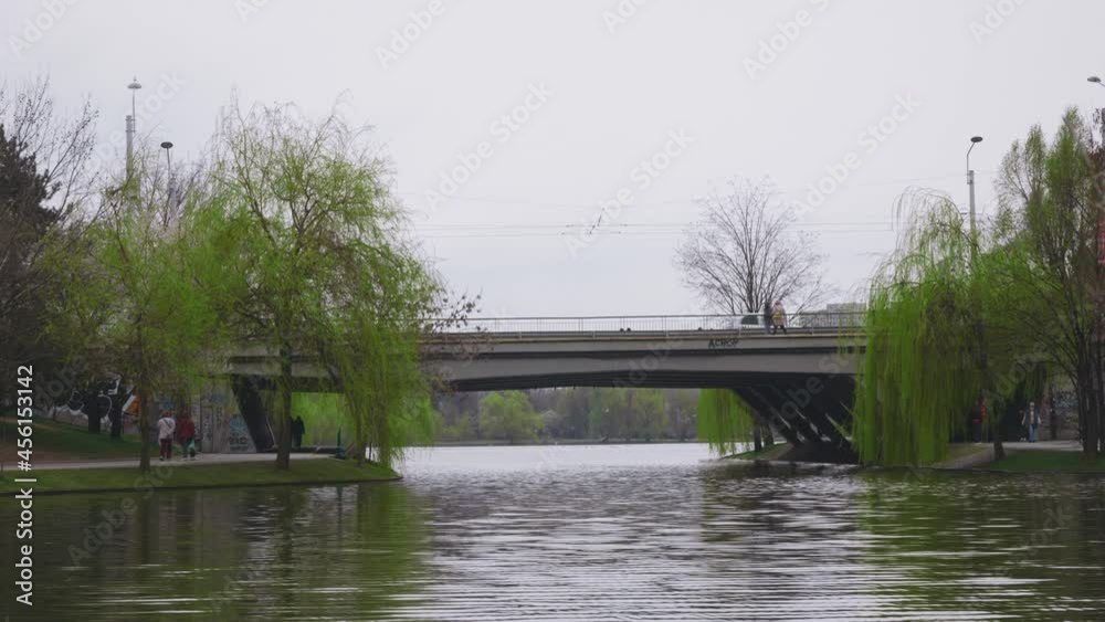 A tram passing left to right on a bridge over a lake. Static shot. A tram passing left to right on a bridge over a lake. Static shot.