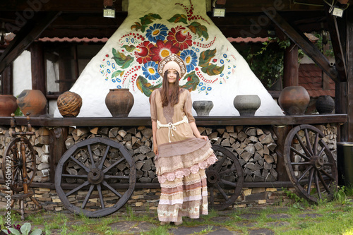 Stylish look of russian girl in traditional national dress (sundress) and slavic headdress - kokoshnik. Russian folk style in fashion. Tourist fashionable woman and wooden house in Russia. A la rus photo
