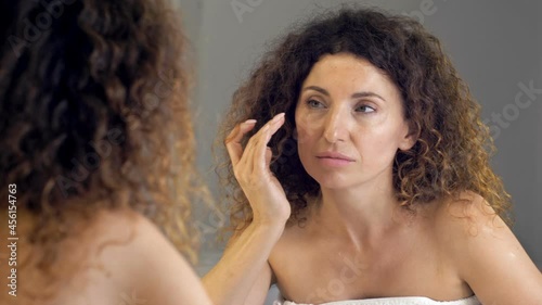 Middle-aged woman regretfully examines her wrinkles in the mirror. photo