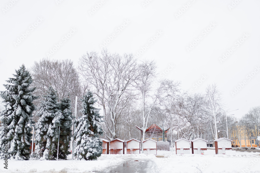 Beautiful winter landscape, trees and closed Christmas market wooden stalls covered with snow.