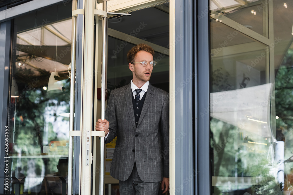 curly businessman in glasses opening door while leaving cafe curly businessman in glasses opening door while leaving cafe
